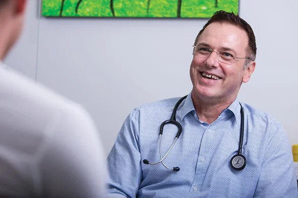 A GP smiling and talking with a patient in a consulting room